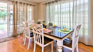 A dining area with a wooden table, white chairs, and a view of the outdoors through large windows.