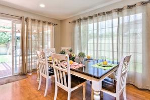 Un espace repas avec une table en bois, des chaises blanches et une vue sur l’extérieur grâce à de grandes fenêtres.