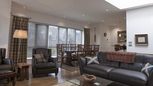 Uma sala de estar moderna com sofá, poltronas, mesa de centro e área de jantar com mesa e cadeiras.