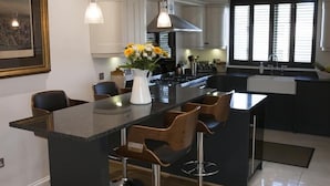 Cozinha moderna com ilha central, banquetas, iluminação pendente e uma grande janela com persianas.