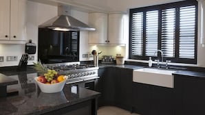 Cozinha moderna com armários escuros, fogão de aço inoxidável, pia e uma fruteira no balcão.