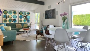 Una sala moderna con un sofá verde, una mesa de centro de vidrio y una zona de comedor con una mesa y sillas blancas.