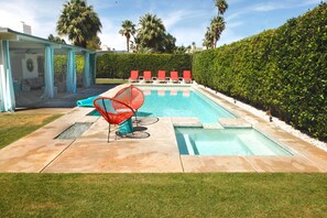 Una piscina con sillas de descanso rojas, un área de estar techada y un césped bien cuidado.