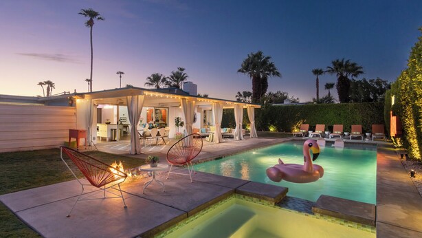 Un área de piscina con una silla en llamas, un flotador de flamenco y una zona de estar cubierta con sillas y una mesa.