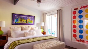 Un dormitorio con cama, almohadas, una lámpara verde, un cuadro enmarcado y una ventana con cortinas.