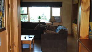 A spacious living room with a wooden ceiling, a sofa, a coffee table, and a window with blinds. - Longview Cottage with views to compliment its name and close to cooperstown (Mount Vision)