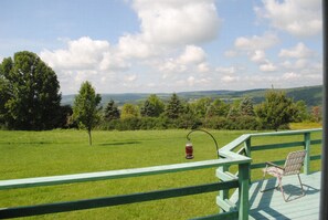 A deck with a chair and a lantern, overlooking a grassy field and trees. - Longview Cottage with views to compliment its name and close to cooperstown (Mount Vision)