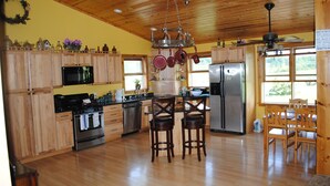 A spacious kitchen with wooden cabinets, stainless steel appliances, and a central island with stools. - Longview Cottage with views to compliment its name and close to cooperstown (Mount Vision)