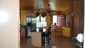 A spacious kitchen with wooden cabinets, a stainless steel refrigerator, and a central island with bar stools. - Longview Cottage with views to compliment its name and close to cooperstown (Mount Vision)