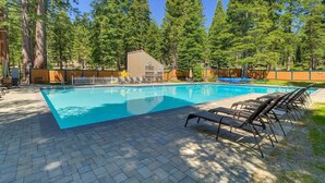 Ein rechteckiger Pool mit gefliestem Sonnendeck, umgeben von Liegestühlen und einer Holzterrasse.