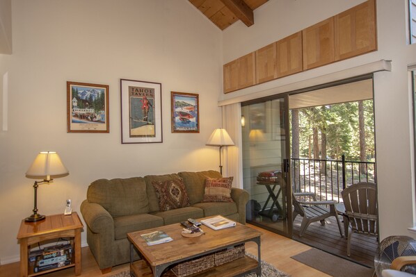 A cozy living room with a sofa, a coffee table, and a glass door leading to an outdoor deck.