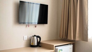 A hotel room with a bed, a desk with a television, a refrigerator, and a chair. - Ace Apartments Hong Kong (Kowloon)