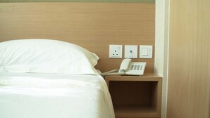 A hotel room with a bed, a bedside table with a telephone, and a wall socket. - Ace Apartments Hong Kong (Kowloon)
