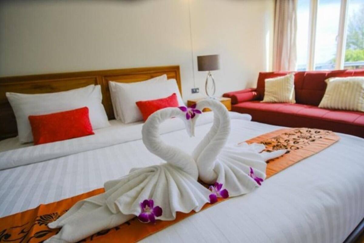 Una habitación de hotel con cama, sofá rojo, televisor montado en la pared y ventana con cortinas.