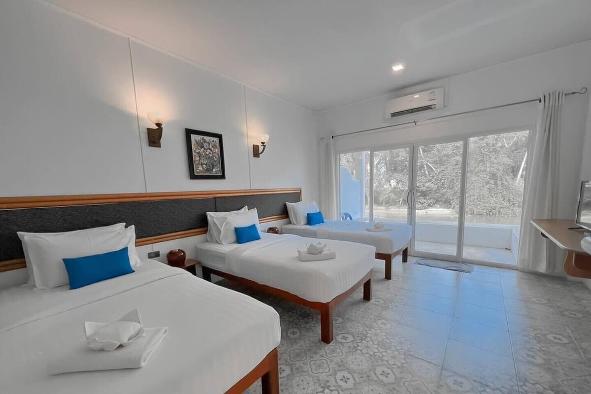 Habitación de hotel con tres camas, un ventanal grande y un equipo de aire acondicionado.