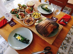 A dining table with various dishes, including a wrapped item on a plate, bowls of food, and a pair of scissors. - Metteyya Healing House (Ubud)