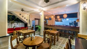 Un restaurante con mesas y sillas de madera, una zona de bar y una escalera que sube a un nivel superior.