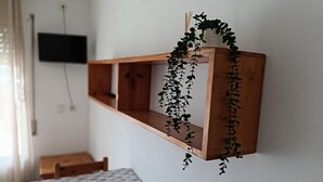 A room with a wooden shelf holding a potted plant, a bed with a patterned bedspread, and a television mounted on the wall. - APCOSTAS Lotus / One Bedroom (Blanes)
