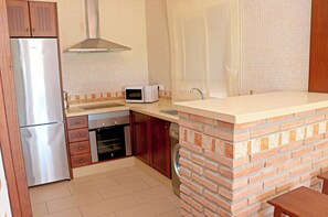 Een kleine keuken met een koelkast, magnetron, oven en een wand met bakstenen.