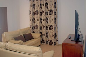 Ein Wohnzimmer mit einer Couch, einem Fernseher auf einem Holzschrank und einem gemusterten Vorhang.
