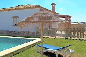 A pool area with a pergola, a lounge chair, and a white building with a tiled roof. - Villa with private pool, town outskirts (CONIL DE LA FRONTERA)