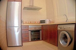 Eine kompakte Küche mit Edelstahlkühlschrank, Mikrowelle, Backofen, Holzschränken und einer Frontlader-Waschmaschine.