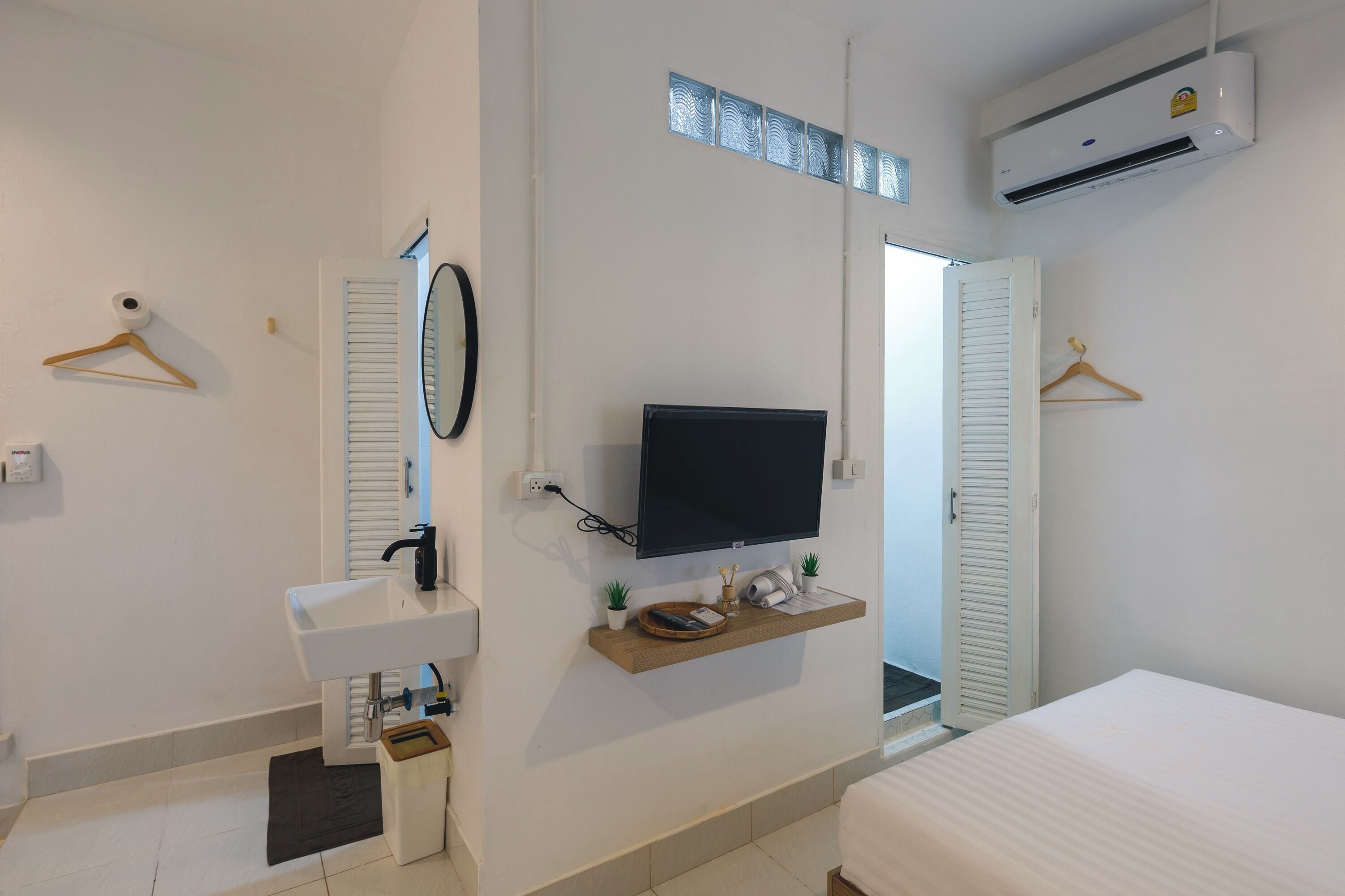 Une chambre d’hôtel avec un lavabo blanc, un téléviseur fixé au mur, une petite étagère avec des objets décoratifs et un lit.