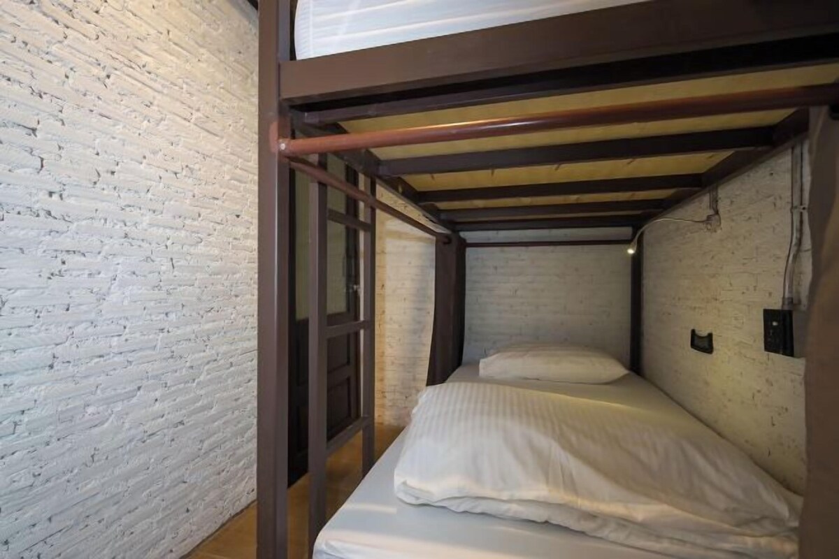 A bunk bed in a narrow room with white brick walls and a wooden ceiling.