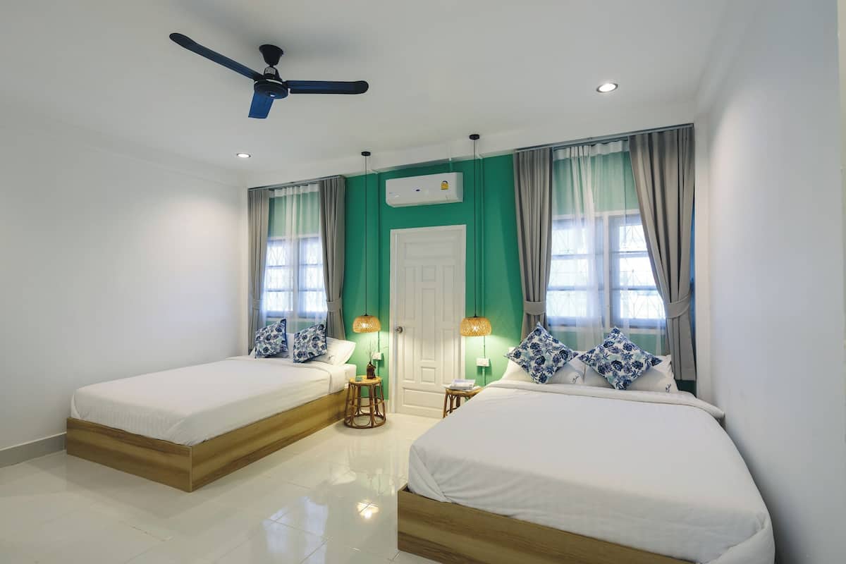Ein Hotelzimmer mit zwei Einzelbetten, einem Deckenventilator, einer Klimaanlage und einer Tür.