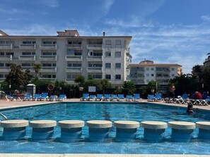 A swimming pool with lounge chairs and a multi-story building in the background.