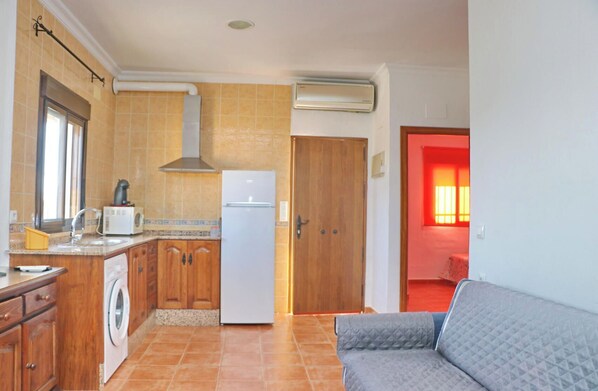 A compact kitchen with wooden cabinets, a washing machine, a refrigerator, and an air conditioner.