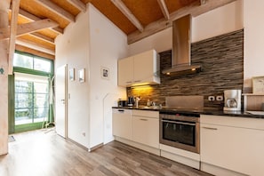 A modern kitchen with wooden beams, a built-in stove, and a large window.