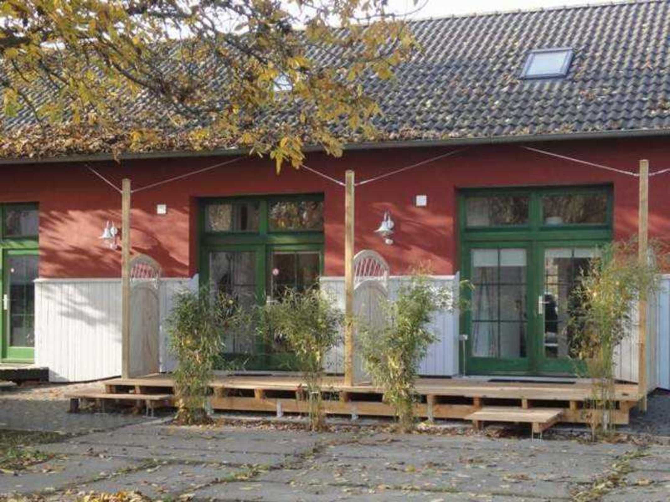 Ein rotes Gebäude mit grünen Türen und Fenstern, einem Ziegeldach und einer kleinen Veranda mit Holzstufen.