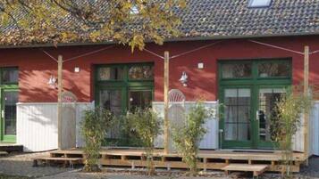 Ein rotes Gebäude mit grünen Türen und Fenstern, einem Ziegeldach und einer kleinen Veranda mit Holzstufen.