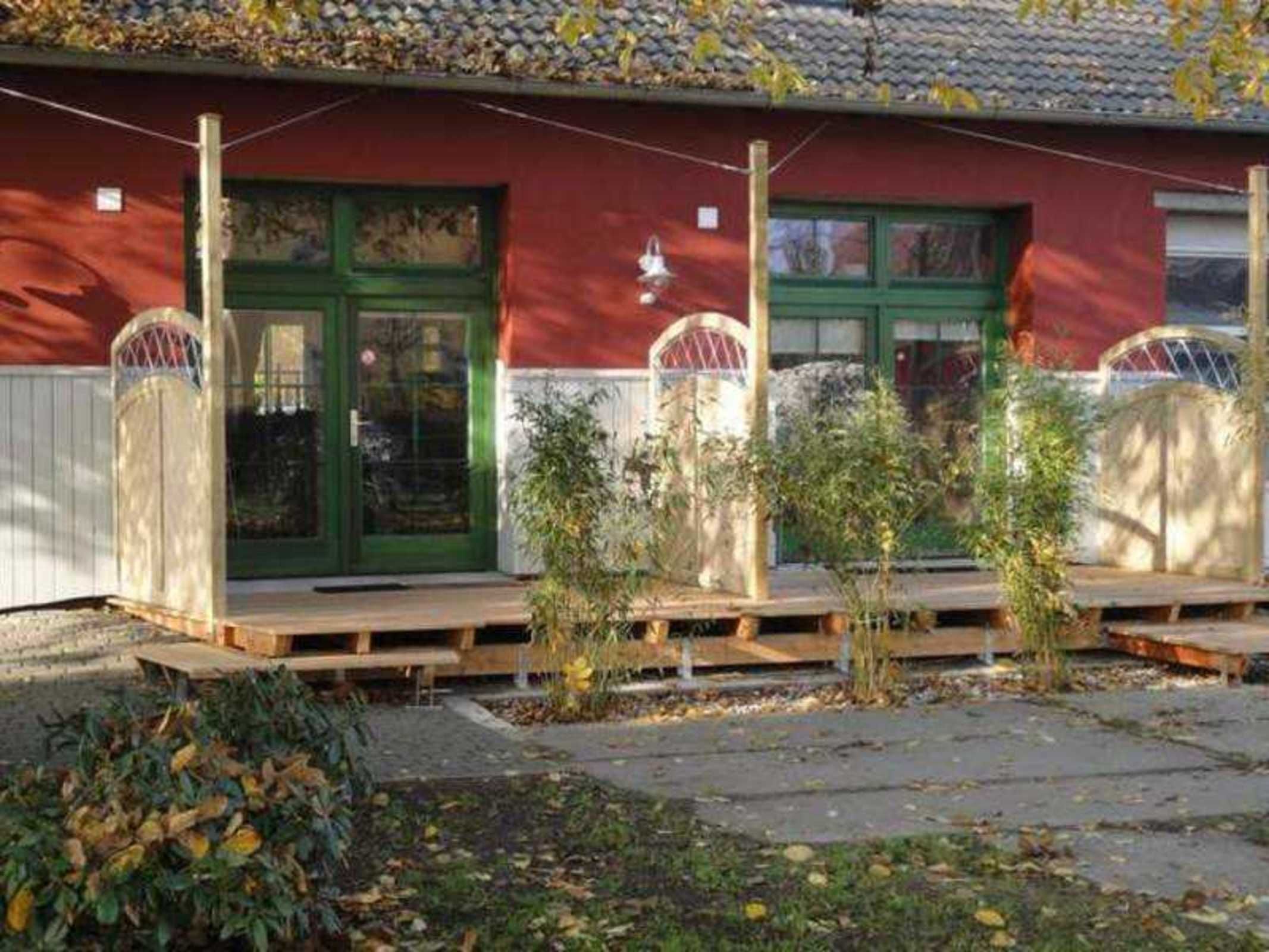 Ein Gebäude mit roter Fassade, grünen Türen und einer kleinen Veranda mit Pflanzen.