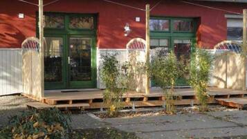 Ein Gebäude mit roter Fassade, grünen Türen und einer kleinen Veranda mit Pflanzen.