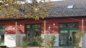 Un edificio rojo con puertas y ventanas verdes, techo de tejas y un pequeño porche con escalones de madera.