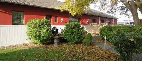 Een rood gebouw met pannendak, omringd door een verzorgd gazon en enkele bomen.