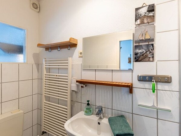 A bathroom with a white sink, a mirror, a towel, and a shelf with toiletries.