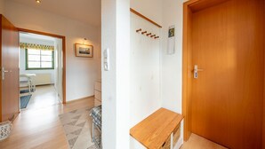 Un pasillo con puerta de madera, un perchero, una mesita y un ventanal con vistas.