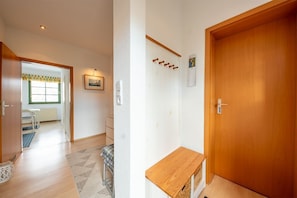 A hallway with a wooden door, a coat rack, a small table, and a window with a view.