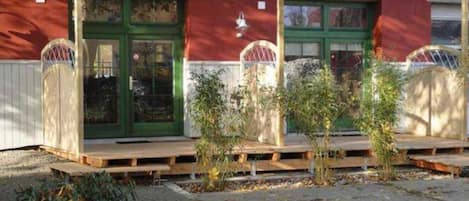 En bygning med rød facade, grønne døre og en lille veranda med planter.