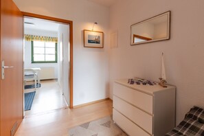 A room with a wooden door, a white dresser, a mirror, and a framed picture on the wall.
