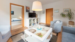 Una sala de estar moderna con una mesa de centro de vidrio, televisor, sofá y una silla.