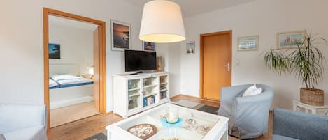 Un salon moderne avec une table basse en verre, un téléviseur, un canapé et un fauteuil.