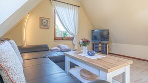 Ett mysigt sovrum på loftvåningen med ett stort fönster, en platt-TV, en soffa och ett litet bord.