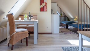 Ett mysigt sovrum på loftvåningen med ett sluttande tak, en matplats med flätade stolar, ett litet bord med en vinflaska och en tavla på väggen.