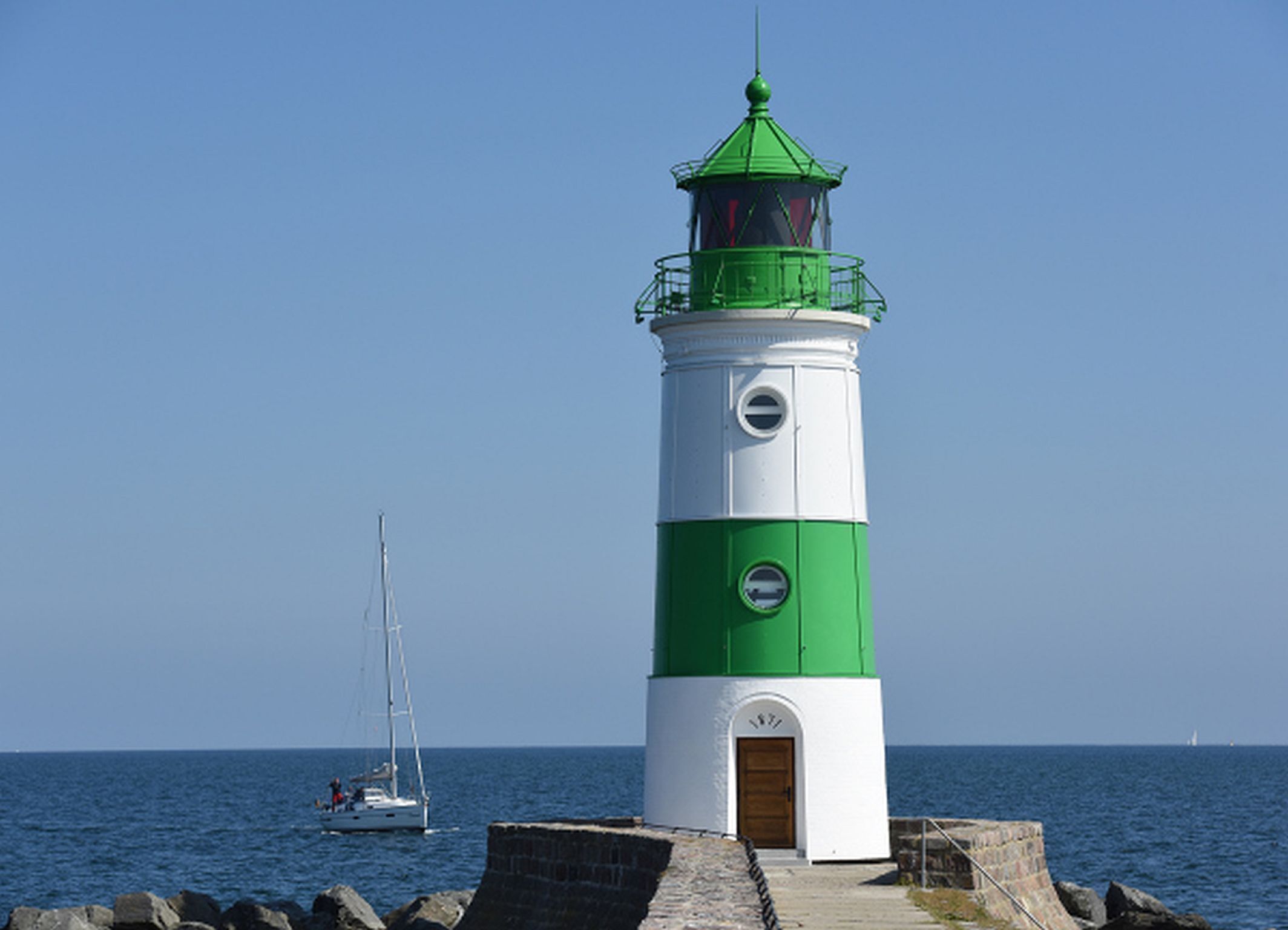 Ein Leuchtturm mit grün-weißer Farbgebung, gelegen an einem felsigen Steg, mit dem Meer im Hintergrund.