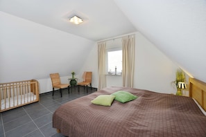 Une chambre à coucher avec un lit, un berceau, deux chaises, une petite table et une fenêtre avec des rideaux.