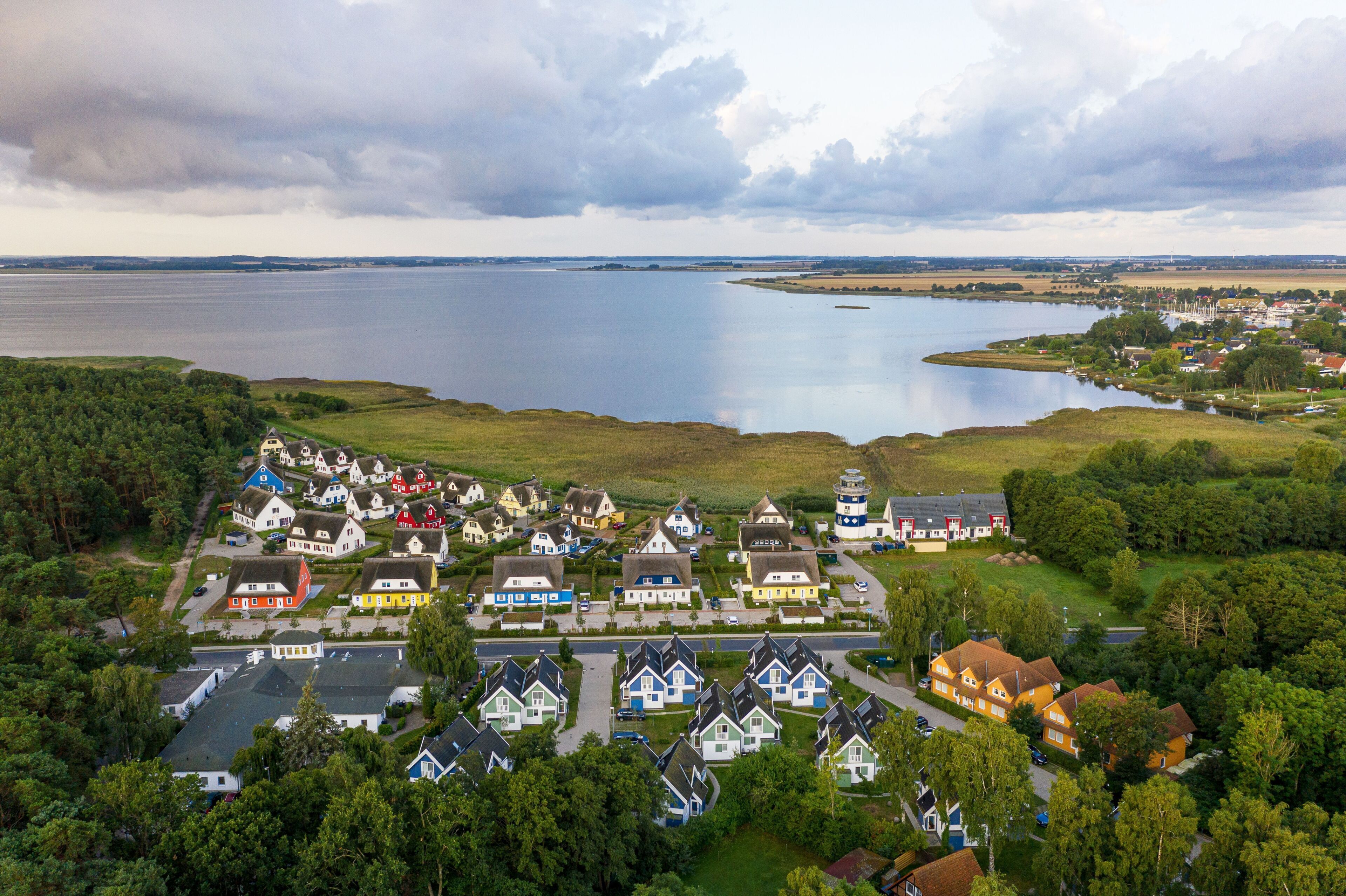 An aerial view of a lakeside village with houses, a lighthouse, and a large body of water.